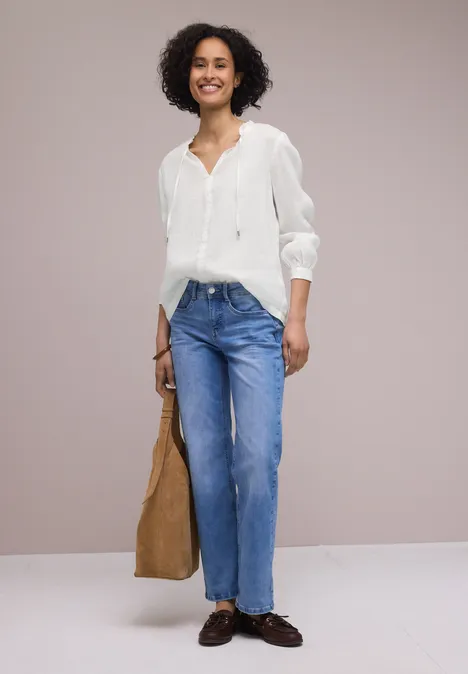 Vrouw in witte blouse, blauwe jeans en bruine loafers met grote bruine tas voor neutrale achtergrond
