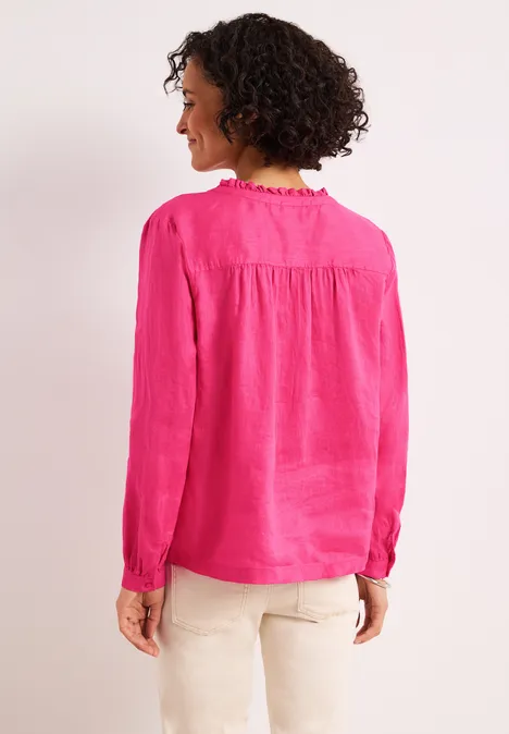 Eine Frau von hinten mit lockigem Haar, die eine pinke Bluse und helle Hosen trägt.