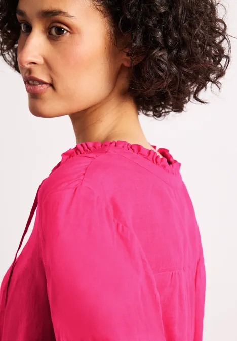 Seitansicht einer Person mit lockigem Haar, die eine pinke Bluse trägt. Das Gesicht ist unscharf.