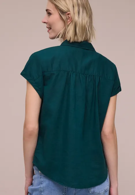 Achteraanzicht van een vrouw met blond haar die een donkergroene, korte mouwen blouse draagt.
