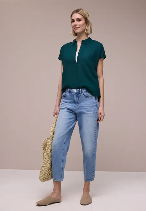 Vrouw met groen T-shirt, blauwe ruime jeans, beige loafers en een gehaakte tas.