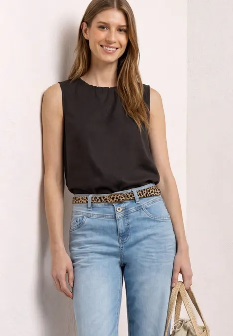 Frau mit schwarzem ärmellosem Top, hellen Jeans, Leoparden-Gürtel und Strohtasche.