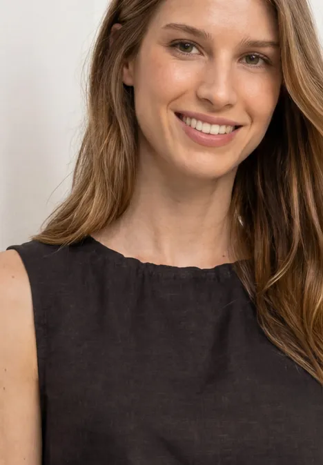 Eine Frau mit langem hellbraunem Haar trägt ein schwarzes ärmelloses Oberteil. Gesicht unscharf.