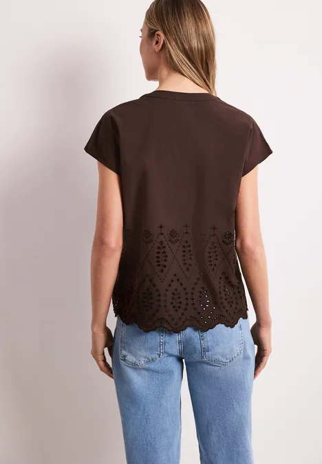 Frau von hinten in braunem T-Shirt mit Lochstickerei-Saum und blauen Jeans.