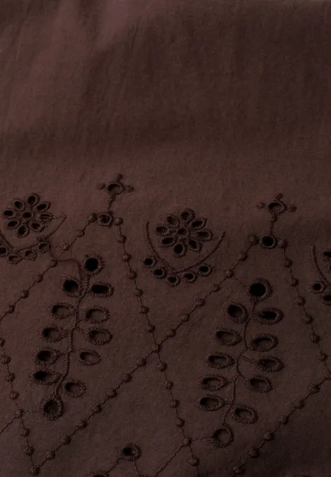 Nahaufnahme eines dunkelbraunen Stoffes mit filigraner Blumen- und Blattstickerei.