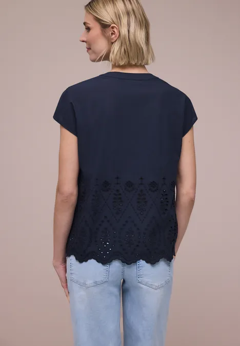 Vrouw van achteren in donkerblauw kort shirt met kantachtige onderrand en lichte spijkerbroek.
