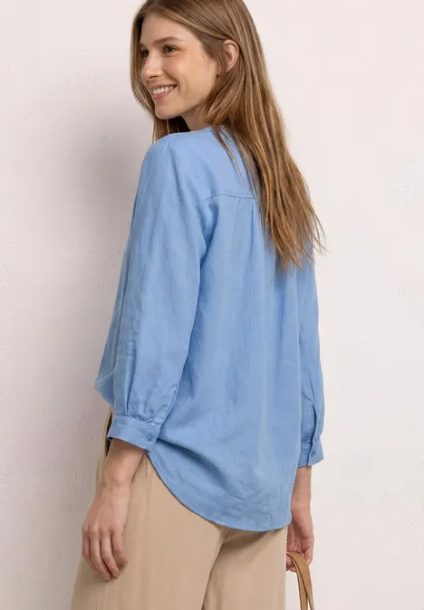 Zijaanzicht van een vrouw in een lichtblauw overhemd, beige broek en met een klein tasje.