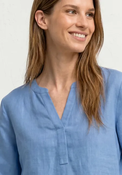 Persoon draagt lichtblauw bloesje met V-hals, gezicht wazig, effen achtergrond.
