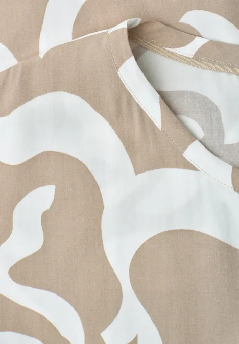 Nahaufnahme eines beigen Stoffes mit weißem, organischem Muster.