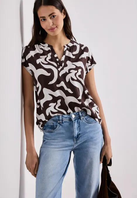 Vrouw met zwart-wit blouse, spijkerbroek en tas voor een lichte achtergrond.