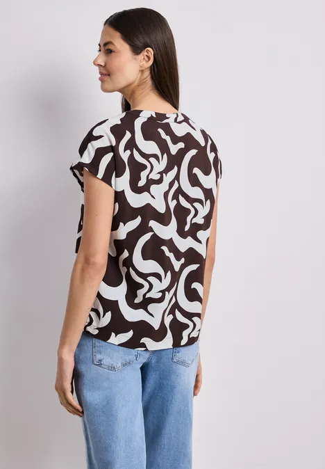 Vrouw van achteren met een kort mouwtop in zwart-wit abstract motief en een blauwe spijkerbroek.