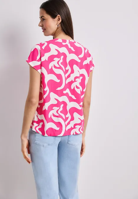 Vrouw van achteren in roze-witte top met dessin en lichtblauwe jeans.