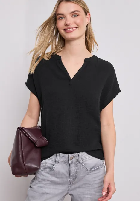 Vrouw met een zwarte blouse, grijze broek en een bordeauxrode tas in de hand.