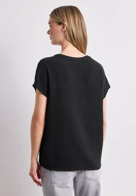 Vrouw van achteren in zwart t-shirt en lichte spijkerbroek voor witte achtergrond.