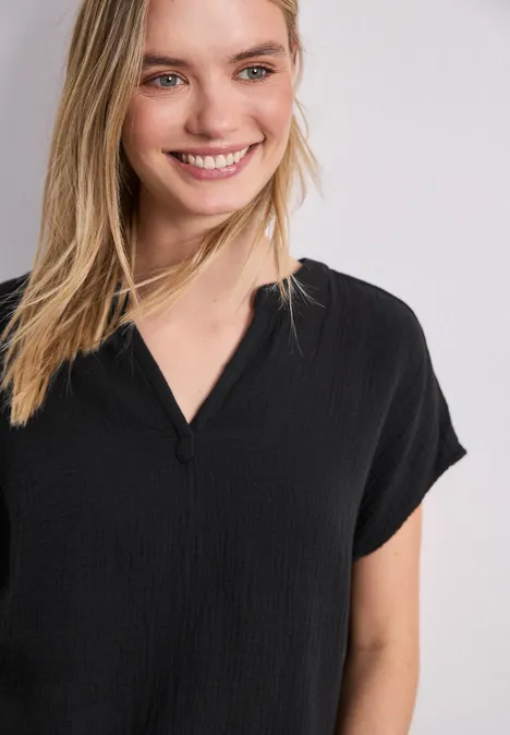 Vrouw in loszittend zwart T-shirt met V-hals tegen witte achtergrond.