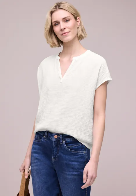 Vrouw in wit shirt en blauwe spijkerbroek, met een bruine leren handtas in de hand.