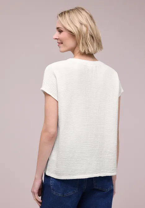 Vrouw van achteren in een wit topje met korte mouwen en spijkerbroek voor een neutrale achtergrond.