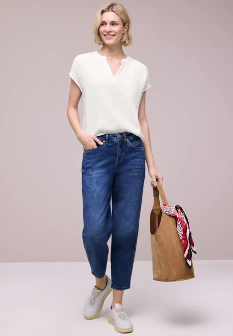 Vrouw met wit T-shirt, blauwe jeans, witte sneakers en rieten tas met rode sjaal.