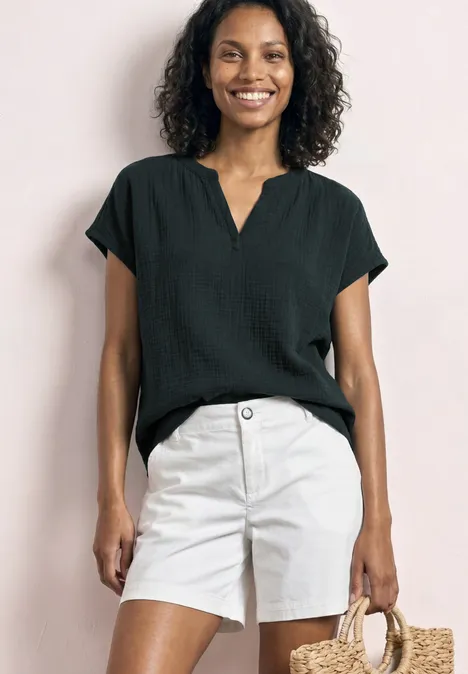 Vrouw in zwarte blouse en witte short met een strooien tas.