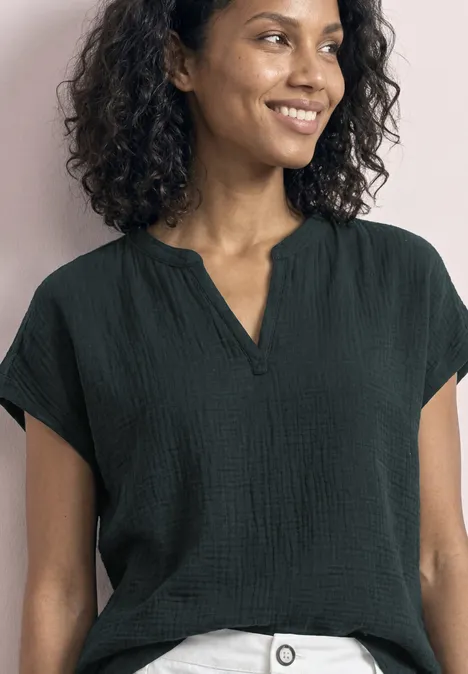 Een glimlachende vrouw met krullend haar draagt een zwarte blouse voor een roze muur.