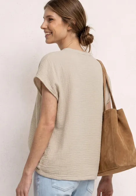 Vrouw van achteren in lichtbeige mouwloos shirt met een bruine suède tas over de schouder.