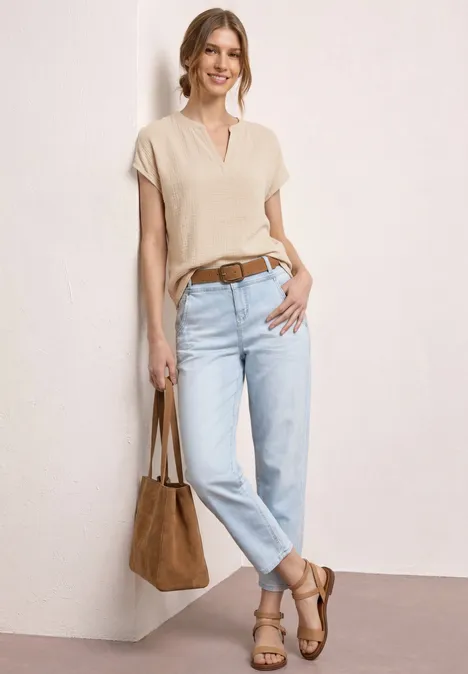 Vrouw in casual look met crèmekleurig shirt, lichtblauwe jeans, bruine riem, sandalen en bijpassende tas