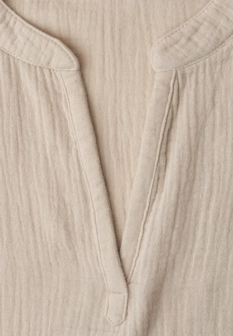 Close-up van een lichtbeige, geribbeld linnenstof met V-hals, vermoedelijk deel van een overhemd of jurk.