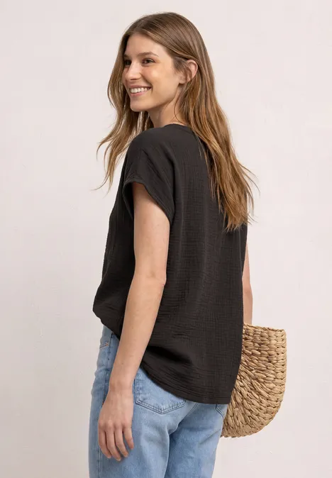 Femme portant un t-shirt noir et un jean bleu clair, vue de côté, avec un sac en paille.