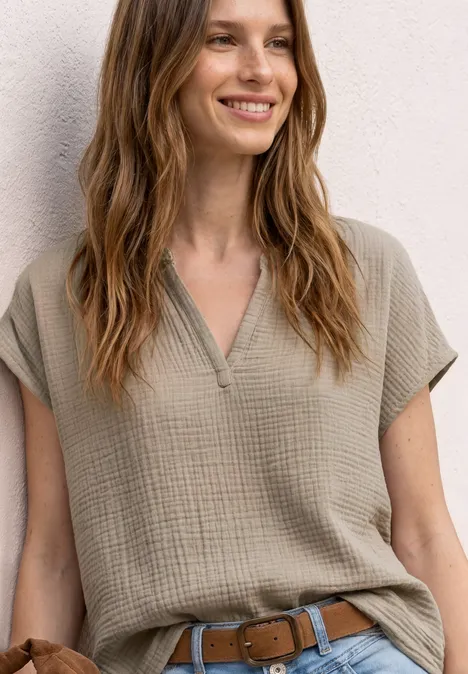 Persoon draagt een kaki top met korte mouwen, V-hals en riem, zachte textuur.