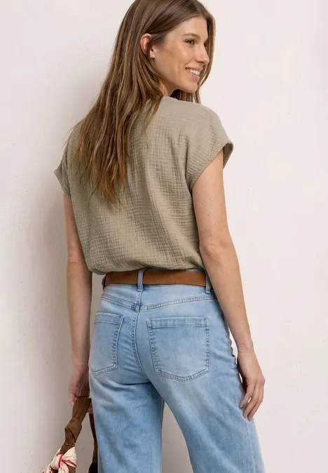 Achteraanzicht van een vrouw in een lichtblauwe jeans, kort shirt en bruine riem, met een tas in haar hand.