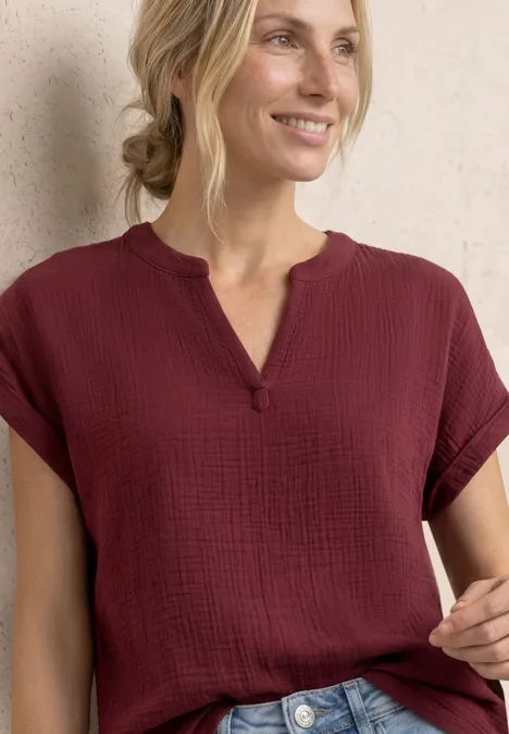 Frau in weinroter, kurzärmliger Bluse mit V-Ausschnitt und texturierter Baumwolle.