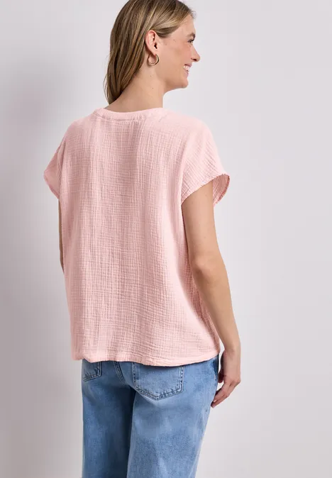 Rugaanzicht van een vrouw in een lichtroze losvallend T-shirt en een blauwe spijkerbroek tegen een witte achtergrond.