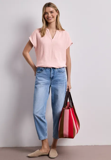 Een vrouw draagt een roze blouse, een blauwe jeans en houdt een rode tas.