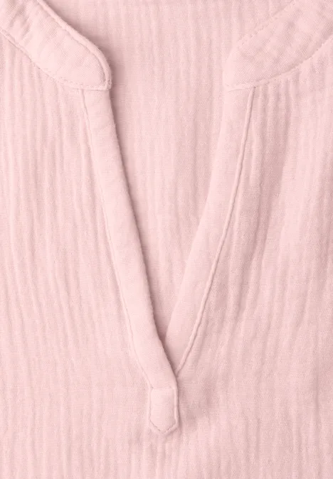 Close-up van een lichtroze bloes van luchtige stof met V-hals en decoratieve knoop.