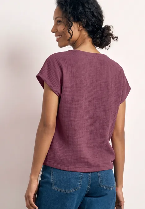 Femme vue de dos portant un t-shirt violet à manches courtes et un jean bleu.