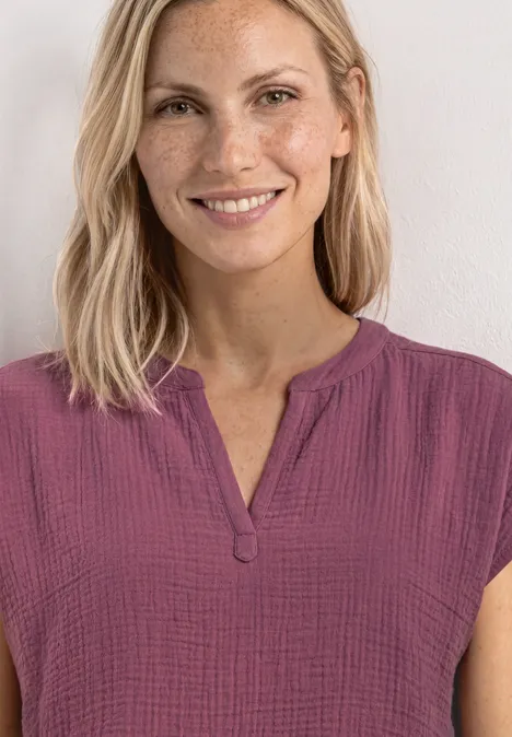 Femme aux cheveux blonds portant un haut court rose violacé à encolure en V.