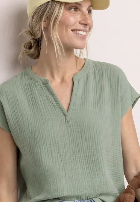 Vrouw in losvallend lichtgroen katoenen shirt met korte mouwen en een subtiele V-hals.