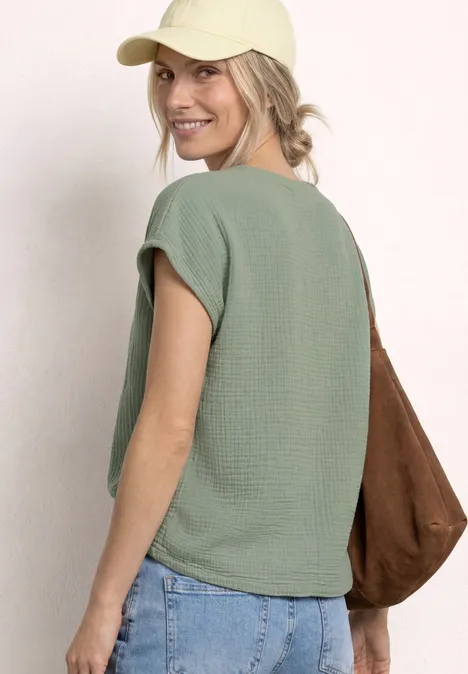 Achteraanzicht van een vrouw met groen shirt, blauwe jeans, gele pet en bruine tas.