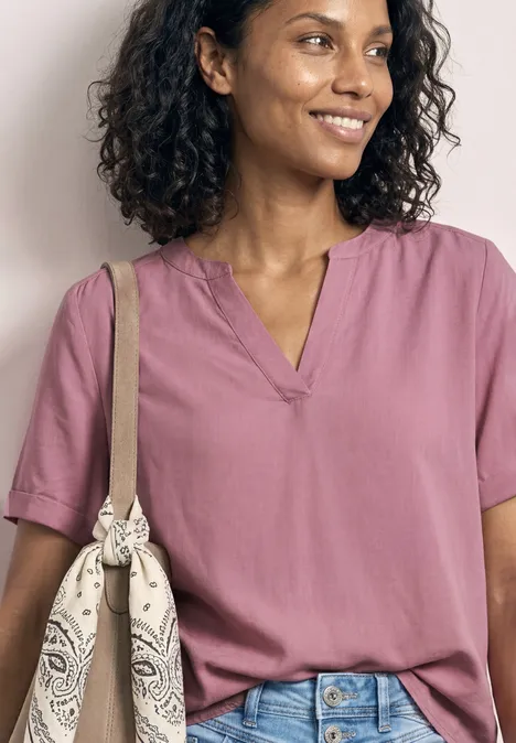 Frau trägt pinkes T-Shirt, blaue Jeans und Umhängetasche mit Bandana-Muster.