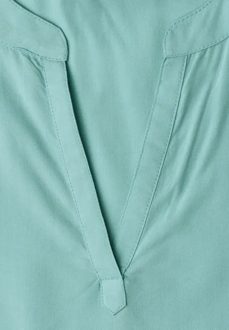 Gros plan d’un haut vert-bleu à encolure en V avec coutures apparentes.