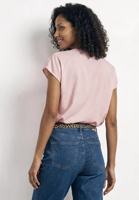 Eine Person von hinten mit rosa T-Shirt, blauer Jeans und Leopardenmuster-Gürtel.