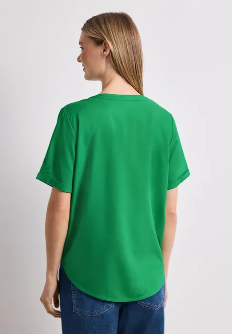 Frau von hinten in locker sitzendem grünen T-Shirt und Jeans vor weißem Hintergrund.