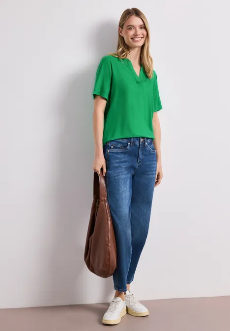 Frau in grünem T-Shirt, blauen Jeans, weißen Sneakern und großer brauner Tasche