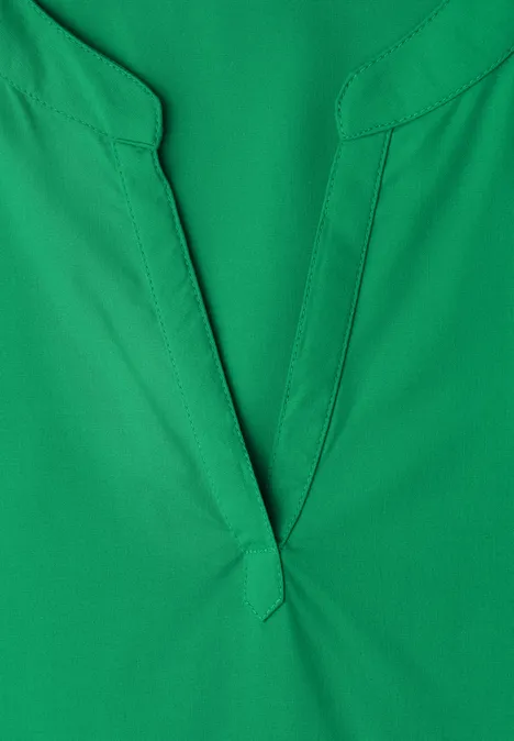 Nahaufnahme eines grünen V-Ausschnitt-Oberteils aus glattem Stoff.