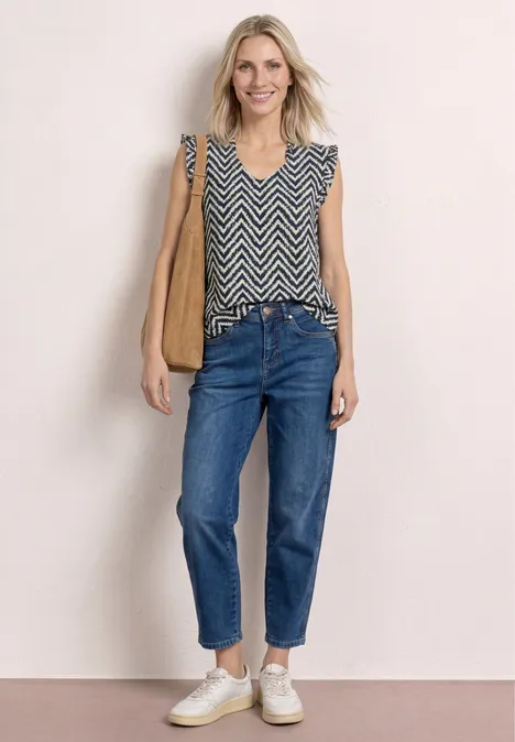 Vrouw in mouwloze zigzagtop, jeans, witte sneakers, bruine schoudertas