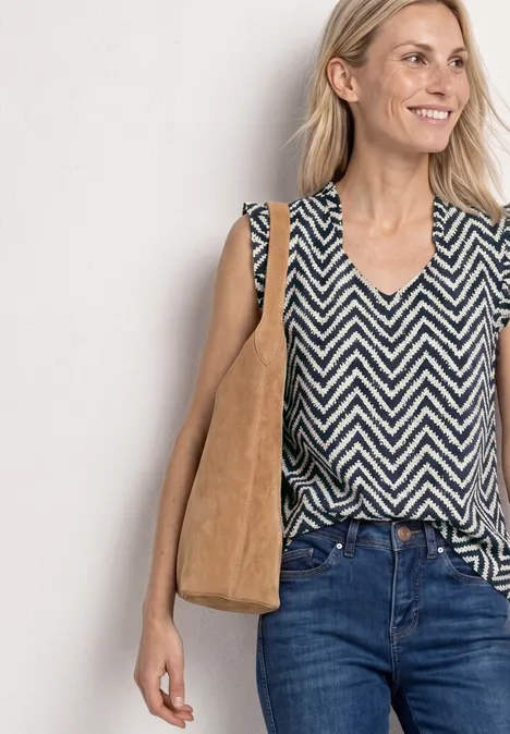 Vrouw in zwart-wit zigzagshirt, blauwe jeans en beige suède schoudertas