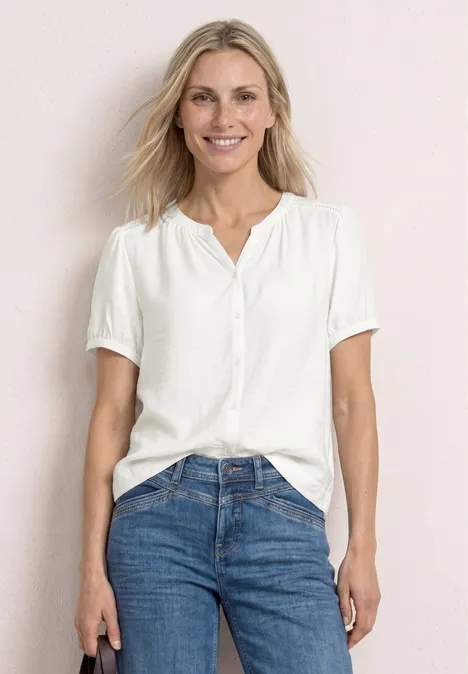 Kurzarm Bluse mit Split Neck und Knöpfen off white Frau in weißer Bluse und blauen Jeans vor hellem Hintergrund.