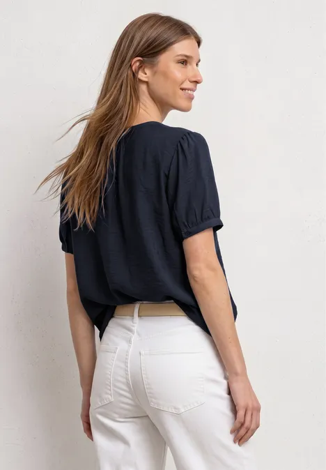 Kurzarm Bluse mit Split Neck und Knöpfen deep blue Frau von hinten mit dunkelblauem T-Shirt und weißer High-Waist-Hose vor neutralem Hintergrund.