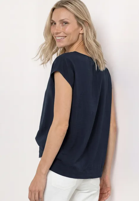 Frau im dunkelblauen ärmellosen Top und weißen Hosen schaut über die Schulter.