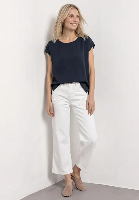 Frau trägt navy T-Shirt, weiße Culotte und beige Stiefeletten vor schlichtem Hintergrund.